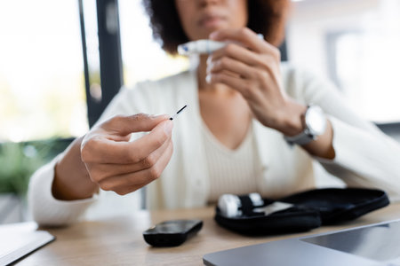 Cropped view of blurred african american woman holding test strip of glucometer in officeの写真素材