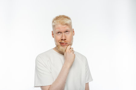 pensive albino man in t-shirt touching beard while thinking on white background