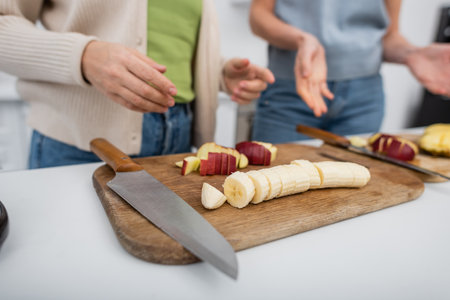 Cropped view of ripe fruits on cutting boards near blurred women in kitchenの写真素材