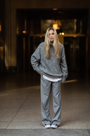 full length of young and stylish woman in grey outfit standing with hand in pocket on street of New...