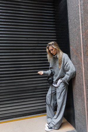 full length of blonde woman in winter outfit standing with hand in pocket and holding handbag outdoorsの写真素材