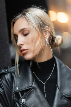 portrait of blonde woman in black leather jacket standing with closed eyes outsideの写真素材