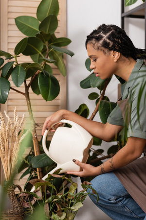 side view of pretty african american florist with trendy hairstyle watering plants in flower shopの写真素材
