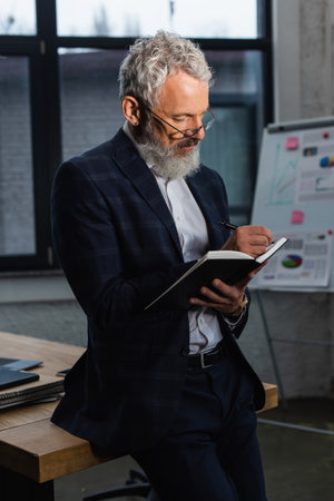 Mature businessman in suit writing on notebook in officeの写真素材