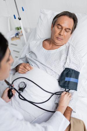 High angle view of blurred doctor using tonometer on elderly patient on bed in clinic