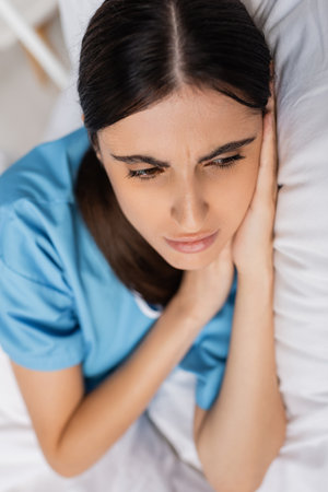 Sick and upset woman in patient gown lying on bed in clinicの写真素材