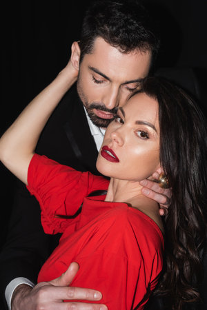 brunette woman with red lips hugging bearded man isolated on black