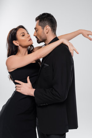 pretty woman hugging bearded man in black suit isolated on grey