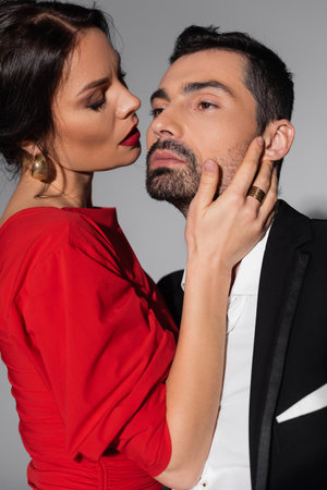Passionate woman with visage touching bearded elegant boyfriend on grey background