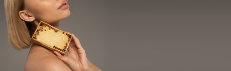 cropped view of blonde young woman holding wooden frame with sweet honey isolated on grey, bannerの写真素材