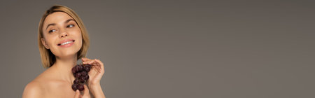 happy young woman holding fresh grapes and smiling isolated on grey, bannerの写真素材