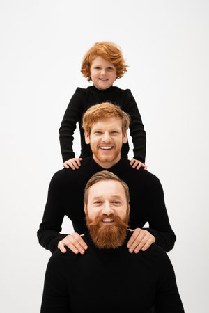 happy redhead boy and bearded men in black turtlenecks looking at camera while posing isolated on greyの写真素材