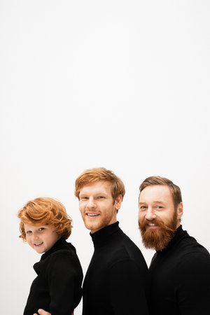 joyful bearded men and redhead boy in black turtlenecks smiling at camera isolated on greyの写真素材