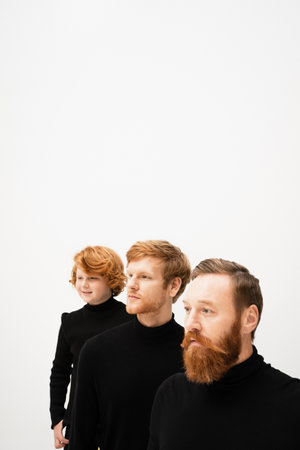 redhead men and happy kid in black pullovers looking away isolated on grey with copy spaceの写真素材