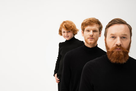 bearded man with redhead son and smiling grandson in black pullovers looking at camera isolated on greyの写真素材
