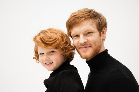 family portrait of redhead dad and son in black sweaters smiling at camera isolated on greyの写真素材