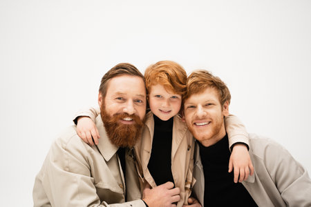 family portrait of redhead boy embracing happy redhead dad and bearded grandfather isolated on greyの写真素材
