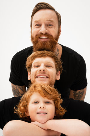 cheerful red haired kid posing with crossed arms near father and bearded grandpa isolated on greyの写真素材
