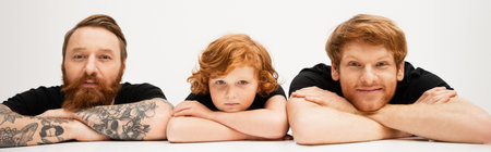 happy man looking at camera near redhead son and bearded tattooed dad lying with crossed arms on light grey background, bannerの写真素材