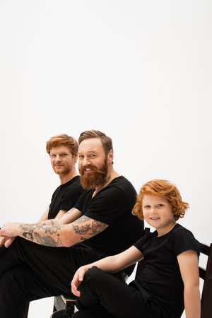 happy redhead boy sitting near bearded tattooed granddad and father isolated on greyの写真素材