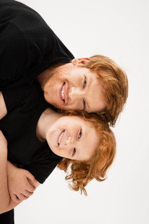 young and cheerful man with redhead son having fun while looking at camera isolated on greyの写真素材