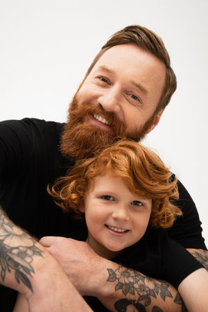 family portrait of red haired boy with bearded tattooed grandpa smiling at camera isolated on greyの写真素材