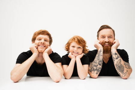 happy boy with redhead father and bearded tattooed grandpa lying and smiling at camera on light grey backgroundの写真素材