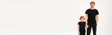 smiling man in black clothes holding hands with red haired son while standing with hand in pocket isolated on grey, bannerの写真素材