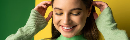 Positive teen girl touching hair on green and yellow background, bannerの写真素材
