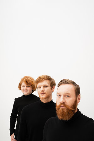 bearded man looking at camera near redhead son and smiling grandson in black turtlenecks isolated on greyの写真素材