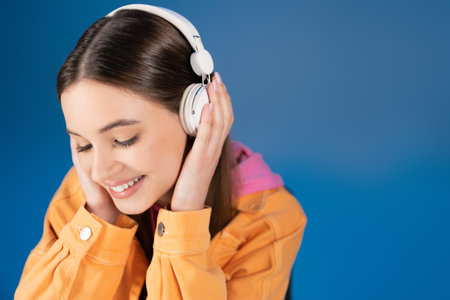 Pretty brunette teenager in headphones listening music isolated on blue