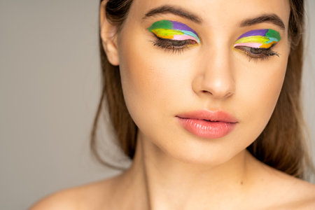 Teenage girl with colorful makeup and naked shoulder looking down isolated on greyの写真素材