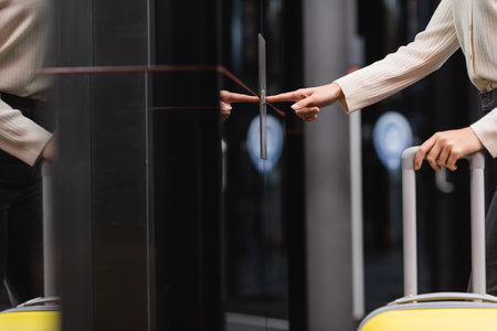 cropped view of woman with travel bag pressing elevator call button in hotel