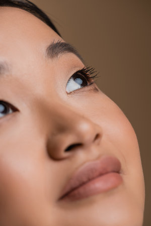 Close up view of young asian woman with visage looking away isolated on brownの写真素材