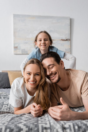 portrait of happy child behind cheerful parents resting in bedroomの写真素材