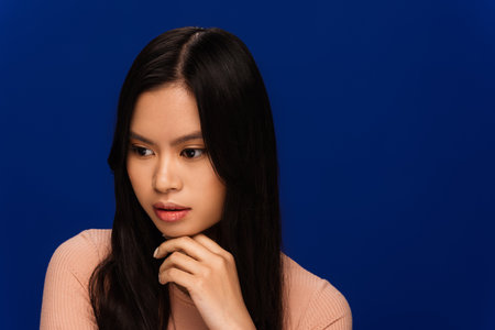 Pensive brunette asian woman looking away isolated on blueの写真素材