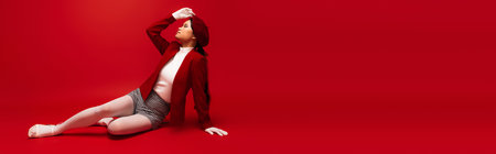Side view of fashionable asian mode posing while sitting on red background, banner