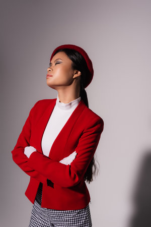 Fashionable asian model in jacket and gloves crossing arms on grey background with shadowの写真素材