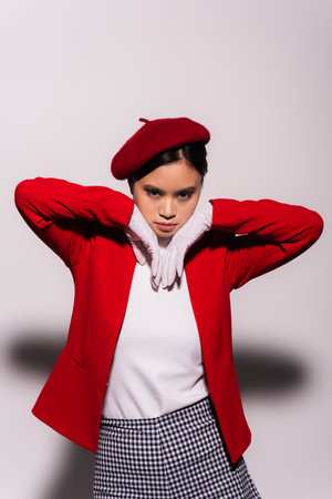 Portrait of fashionable asian model in red and white clothes looking at camera on grey backgroundの写真素材