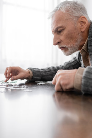 side view of aged man with parkinson syndrome combining jigsaw puzzle at homeの写真素材