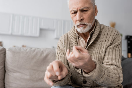 worried senior man suffering from parkinsonian syndrome and looking at trembling hands on blurred foregroundの写真素材