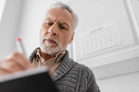 low angle view of grey haired man with alzheimer syndrome writing in blurred notebookの写真素材