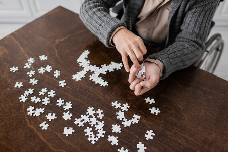 partial view of disabled man with parkinson disease holding elements of jigsaw puzzle in trembling...