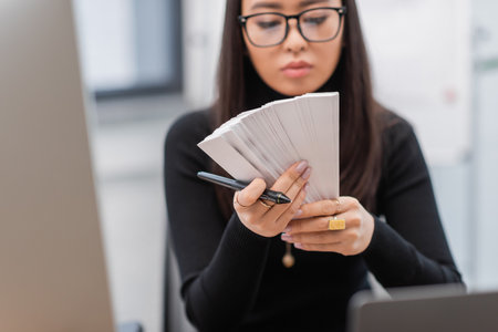 Blurred asian interior designer holding color samples near devices in officeの写真素材
