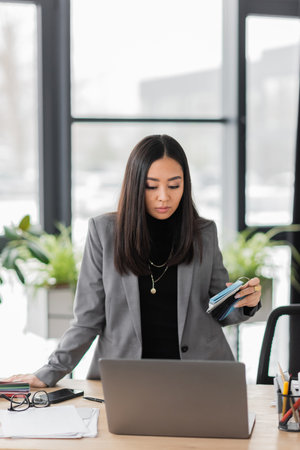 Asian interior designer holding color samples near laptop and eyeglasses on working tableの写真素材