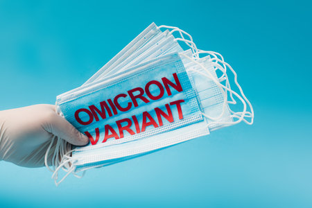 Cropped view of doctor in latex glove holding medical masks with omicron variant lettering isolated on blueの写真素材