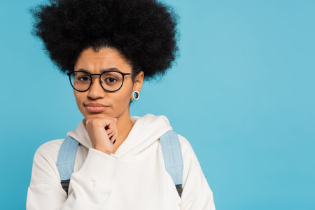 upset and thoughtful african american student in eyeglasses holding hand near chin and looking at...