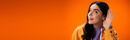 Smiling brunette woman listening isolated on orange, bannerの写真素材
