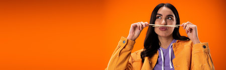 Pretty brunette woman holding chopsticks and pouting lips isolated on orange, banner