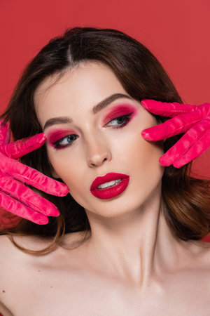portrait of young woman with magenta color eye makeup posing in bright gloves isolated on pinkの写真素材